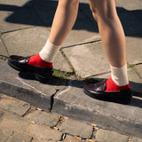 Person wearing red shoes and white socks walking on a stone pavement.