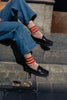 Person wearing blue jeans, black loafer shoes, and striped socks sitting on a stone step.