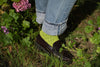 Person wearing green socks and black shoes with rolled-up jeans standing in a garden.
