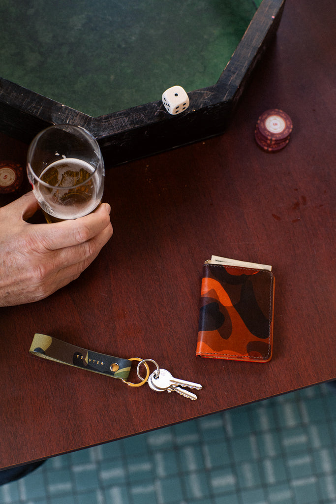Orange camouflage leather slim wallet. Handmade in Portugal from Italian vegetable tanned leather. With ESCUYER branding inside. Camouflage-patterned wallet with brown, black, and orange colors.