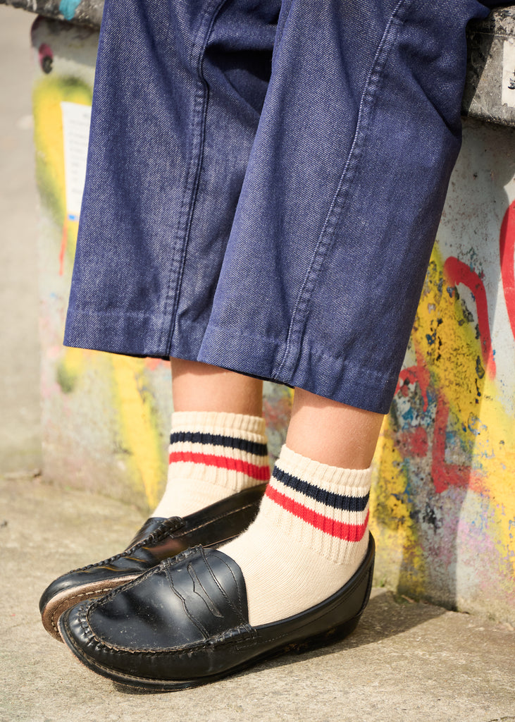 Person wearing blue shorts, black shoes, and striped socks against a colorful wall.
